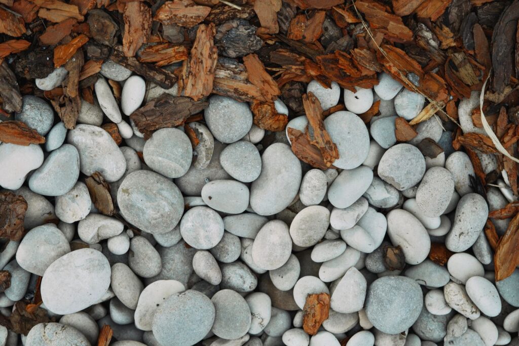 Smooth stone mulch pebbles beside shredded bark mulch chips, showing the texture contrast clearly