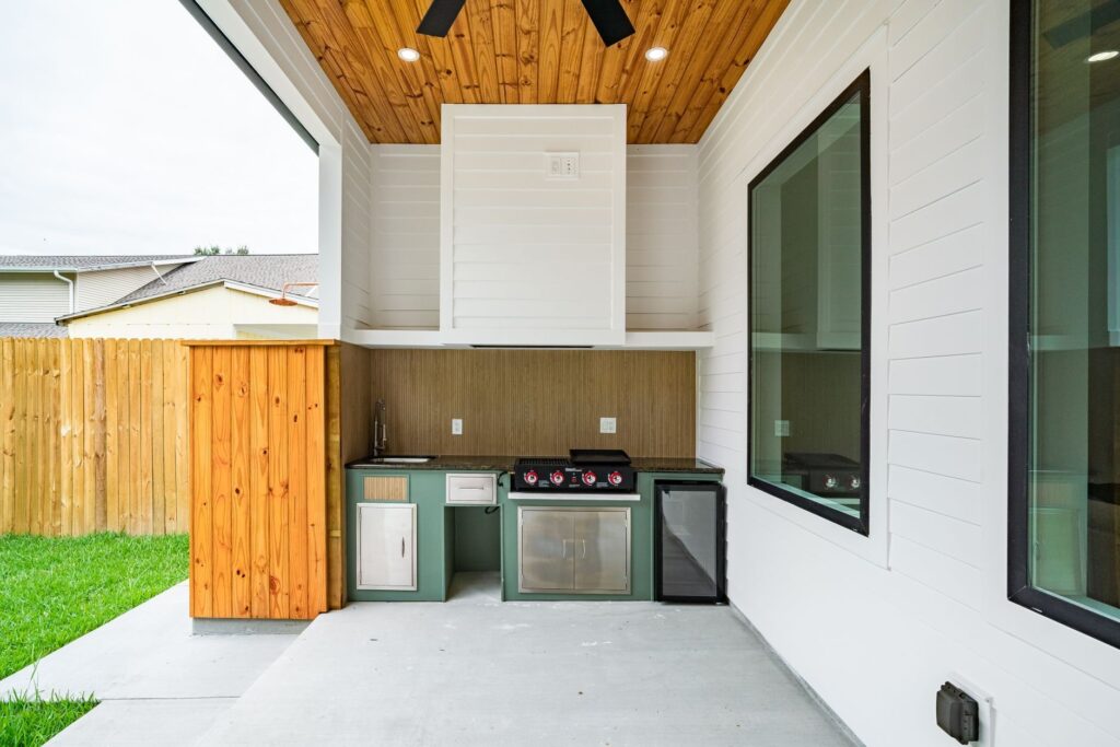 Built-in outdoor kitchen with grill, sink and cabinets under a covered backyard patio