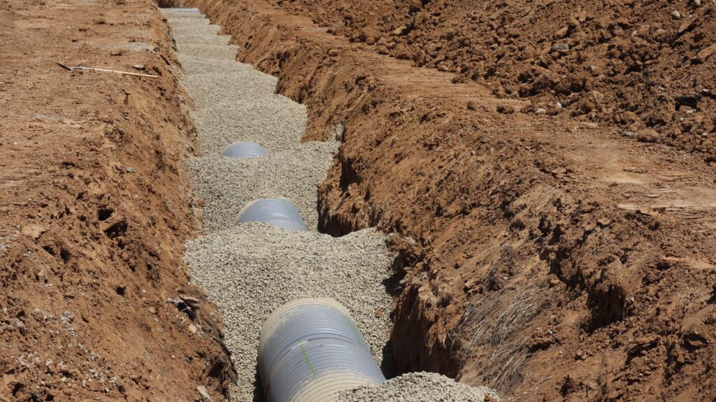 Drainage pipe laid in a gravel trench, the kind of grading work a backyard hardscape needs