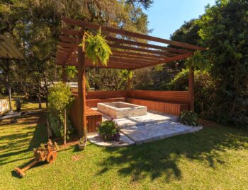 Freestanding wood pergola over a stone patio and fire pit in an open backyard lawn