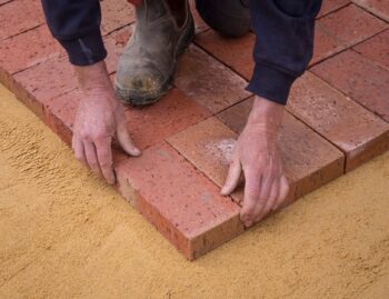 Crew hand-setting brick pavers into a compacted sand base, R&G Almanza paver patio installation